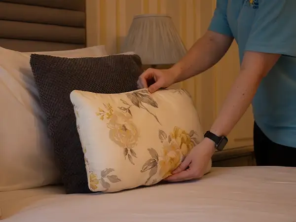 A woman thoughtfully placing a cushion on an elegantly made bed adorned with linen hire. 
