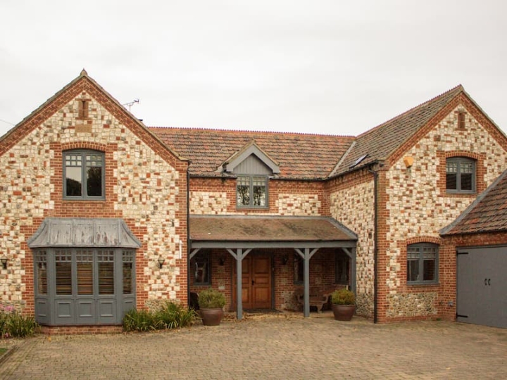 A picturesque second home in Norfolk, surrounded by serene natural surroundings, highlighting a clean driveway and patio, smear-free windows, and well-maintained gutters and fascias for a tidy and welcoming appearance.
