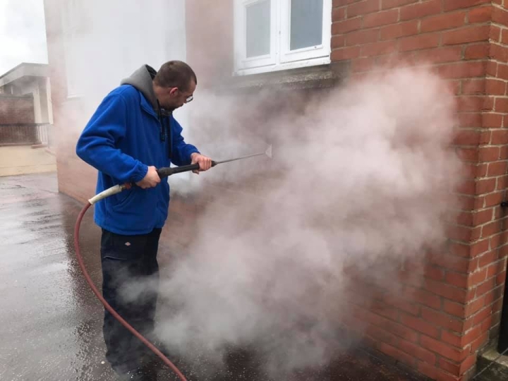 Professional cleaning operative utilising high-temperature, high-pressure liquid spray to effectively break down graffiti paint, meticulously restoring surfaces of this former glory building.